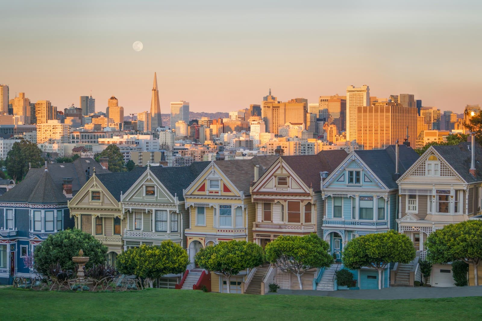 A row of Victorian houses in San Francisco at golden hour, with the downtown skyline behind them.