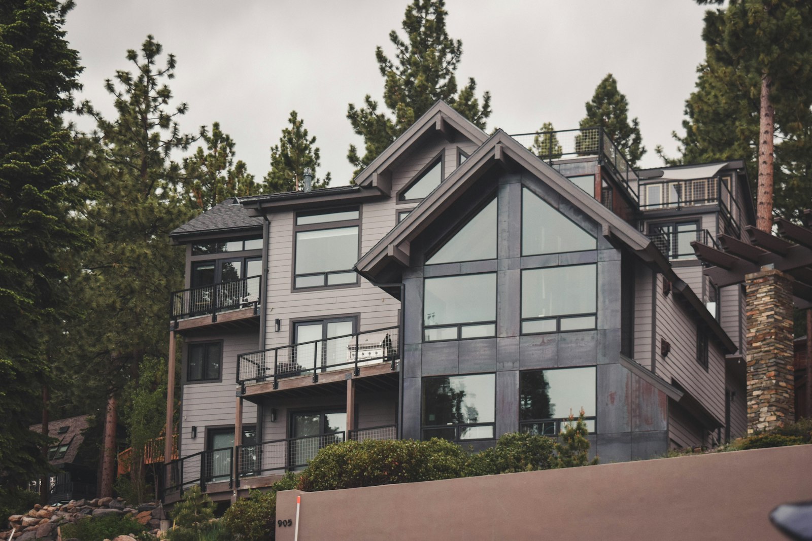 A multi-story mountain home with tall windows and wood siding set among pine trees near Lake Tahoe.