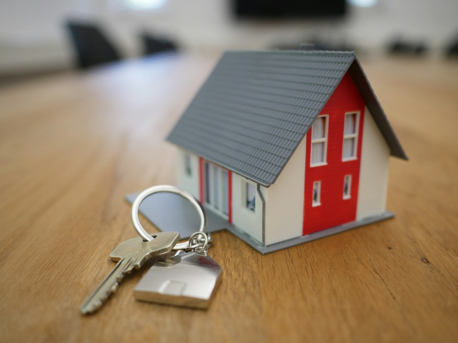A set of house keys resting beside a small model home on a wooden table.