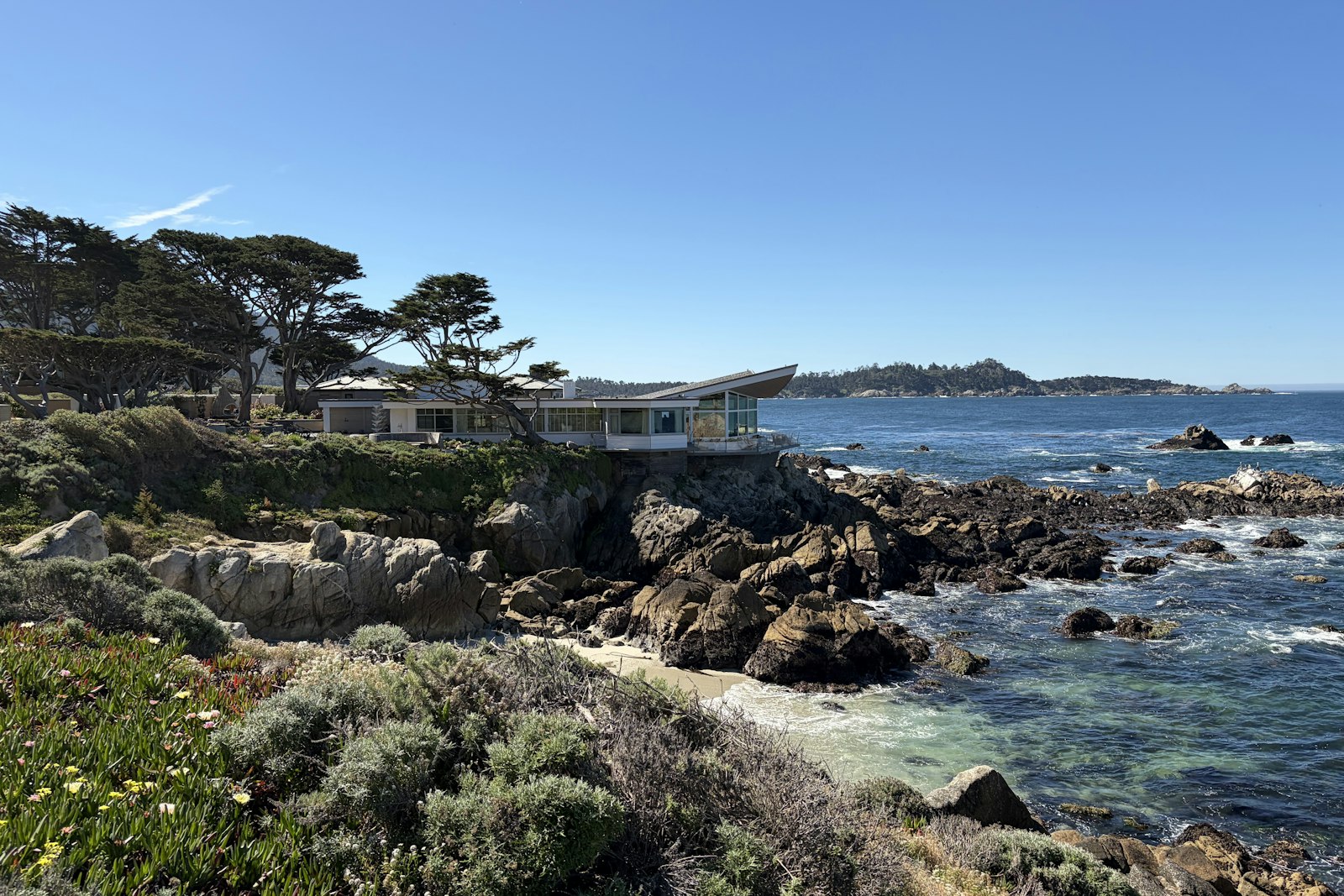 A modern home above a rocky cove on the Monterey Peninsula coastline on a clear day.
