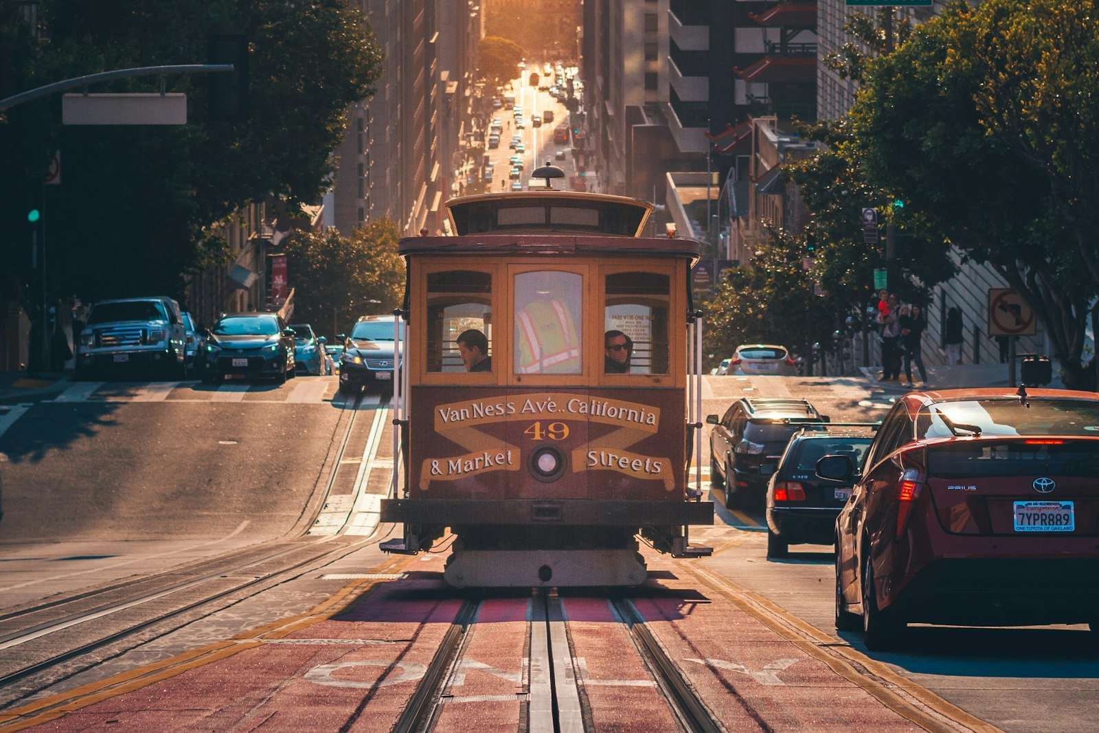 A San Francisco cable car climbing California Street at sunset between parked cars.