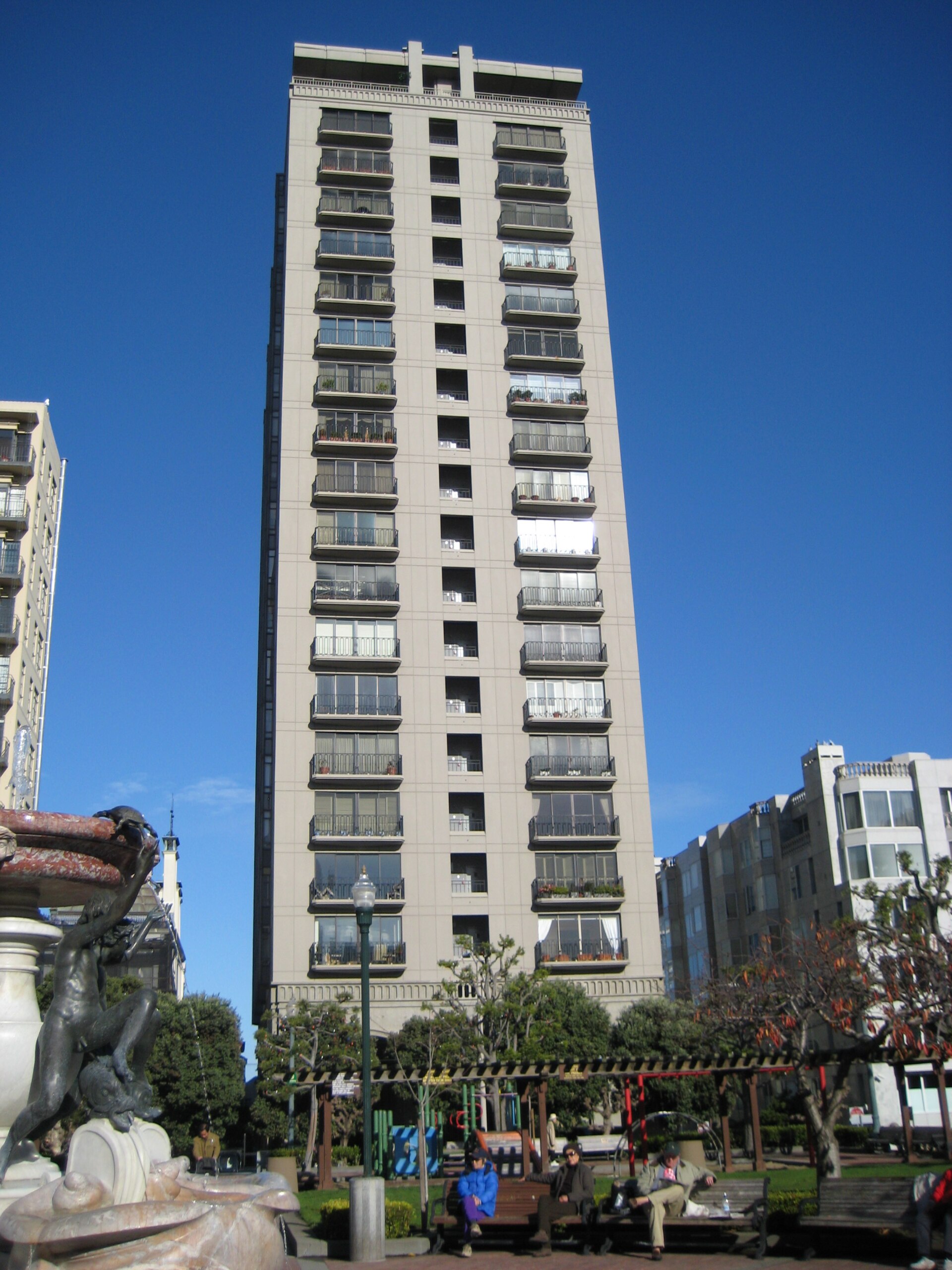 A tall residential tower with rows of balconies above a small park on Nob Hill in San Francisco.